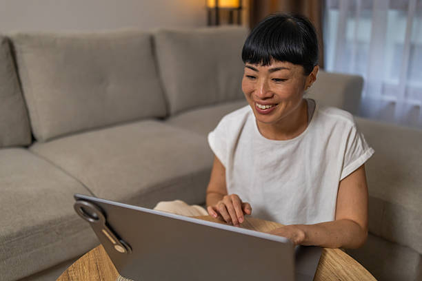 istock Smiling Japanese woman searching the web, using laptop while sitting at the table in the dining room. 2244274543