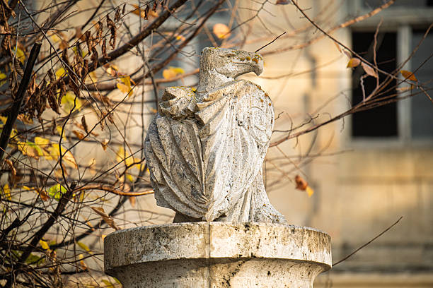 A statue of eagle on a pedestal. The birds are facing each other and appear to be in a moment of contemplation. The scene is set against a backdrop of trees and buildings