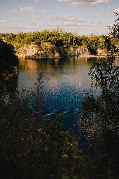 istock Golden hour sunlight reflecting on Zakrzowek lagoon with trees and cliffs in background, creating serene and peaceful atmosphere in Krakow, Poland. Golden hour on Zakrzowek lagoon, cliffs and trees 2244278551