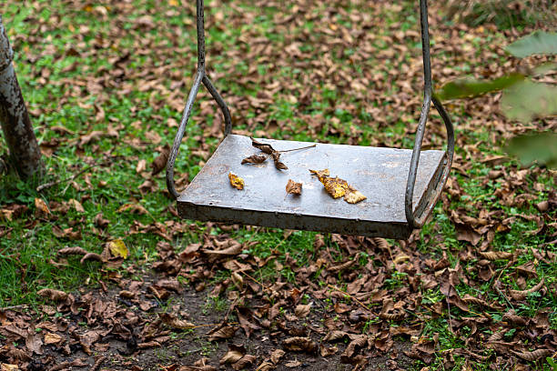 Forgotten Childhood: Close-up of an Empty Swing with Rusted Chains and Autumn Leaves.