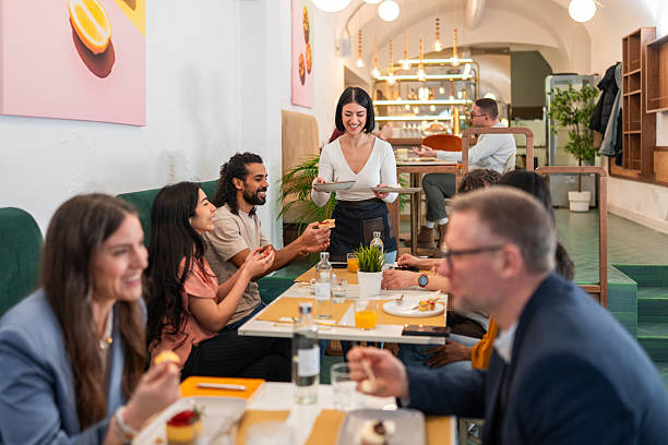 istock Caucasian Waitress Serving Desserts to Diverse Diners in a Bright Cozy Bistro 2244279219