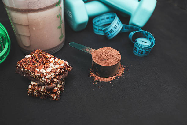 istock Chocolate whey protein powder scoop, protein shake in shaker bottle, protein bar, dumbbells, measuring tape on dark background, sport nutrition and healthy lifestyle concept 2244279984