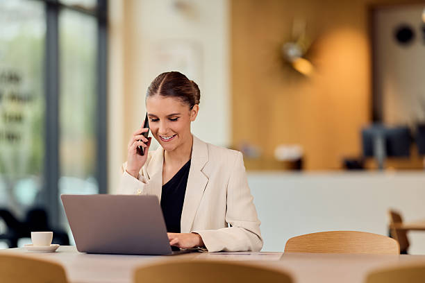 istock Professional Businesswoman Multitasking On Laptop And Phone In Bright Modern Cafe Setting 2244280340