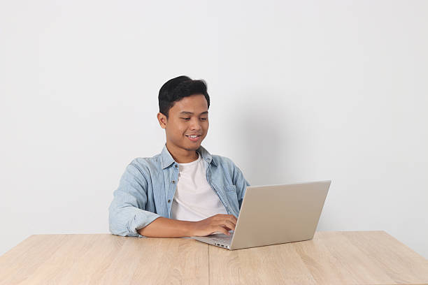 istock Confident Asian man smiling and working on his laptop, enjoying his tasks, isolated on white background 2244281068