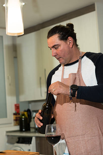 istock Man opening red wine bottle during cooking in kitchen 2244282375