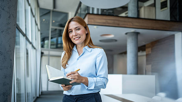 istock Businesswoman standing in modern office holding notebook smiling 2244283977