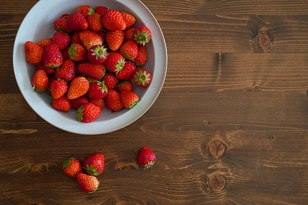 A plate filled with fresh strawberries placed on a rustic wooden table, showcasing their vibrant red color.