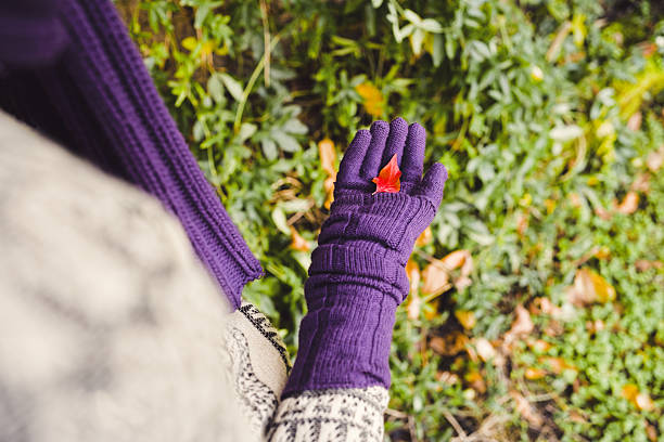 Close-up/over the shoulder view of a red leaf resting on purple gloves, teenager holding a red leaf. The contrast of colors and textures conveys tranquility, introspection and gratitude for simple seasonal beauty, celebrating warmth and connection to nature. Copy space for text, high angle view - Winter, lifestyle