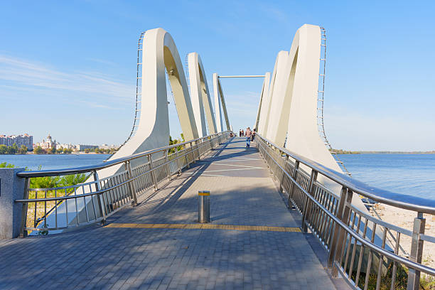 Kyiv, Ukraine - September 23, 2025: Vibrant scene of individuals walking on the Wave Bridge, enjoying the stunning cityscape and river views in Kyiv.