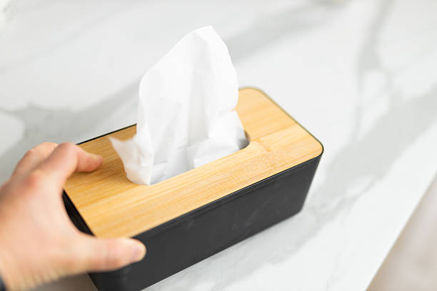 istock Hand grabbing tissue from black and wood dispenser on marble surface 2244294060