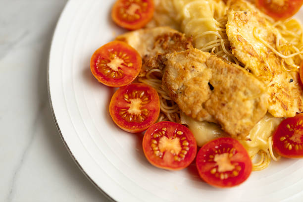 Grilled chicken with pasta and sliced cherry tomatoes on white plate.