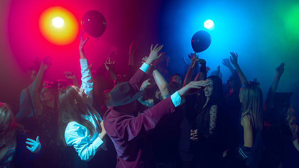 People reaching for black balloons at neon Halloween dance floor. Concept of fashion and style, psychology of euphoria, youth celebration and modern spooky advertising.