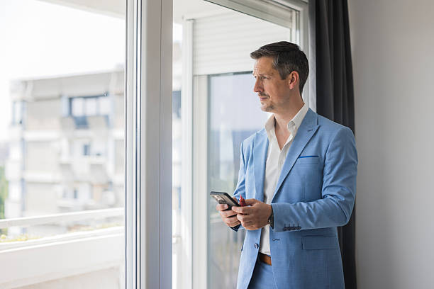 istock Thoughtful businessman holding smartphone looking out apartment window 2244302468
