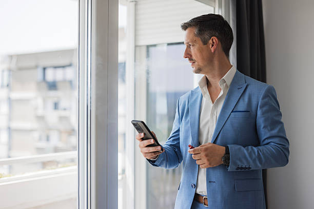 istock Businessman looking out window holding smartphone and pen 2244302479