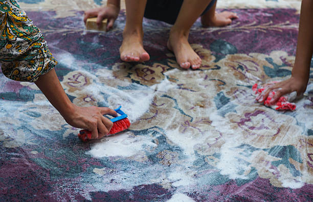 A washing basin filled with soapy water sits on a striped towel. A blue sponge floats on the surface, while a pair of turquoise gloves are ready for cleaning.