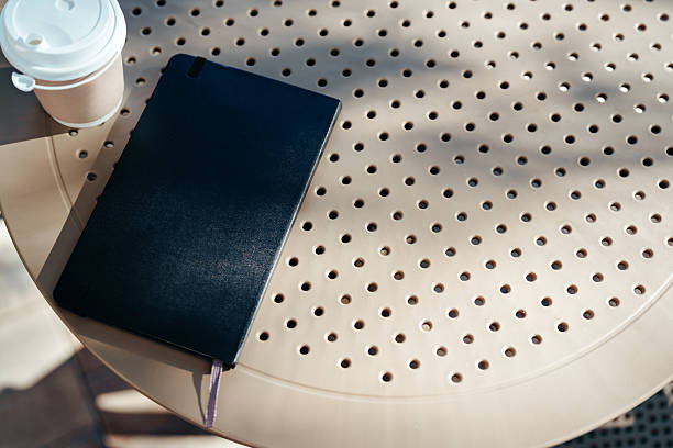 istock Notebook and coffee cup resting on a round table in a sunny outdoor cafe setting 2244309375