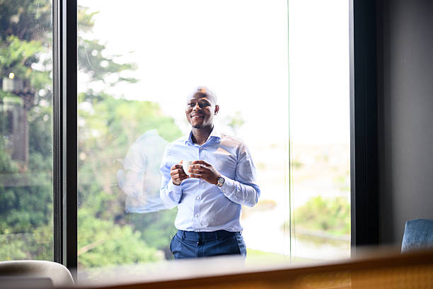 istock Smiling businessman standing by large office window holding smartphone in a modern premium workspace with green outdoor views 2244310480