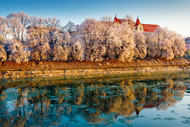 uzhhorod, ukraine - 10 jan 2010: uzh river in the old city in winter. cityscape with hoarfrost on the embankment. european urban landscape with school building reflecting in the water with ice