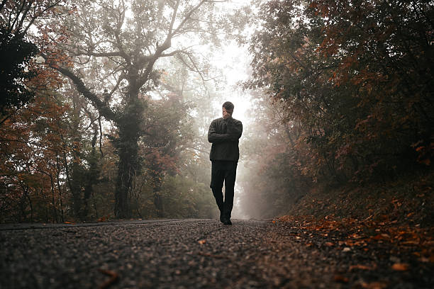 Young adult man walking along a gravel road in a misty forest during autumn