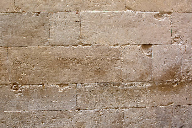 Close-up of a beige limestone wall. An ancient inscription, almost erased by time, is hidden on a central block, suggesting history and mystery.