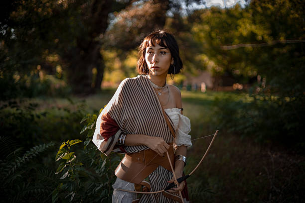 Young woman archer walking through autumn forest with bow and arrow, fall colors inspiration and focus concept