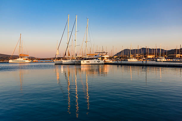 Sea harbor at dawn. The sky, painted golden by the rising sun, is reflected in the calm ripples of the sea. The yachts stand out in beautiful silhouettes against the sky, bathed in the light of dawn.