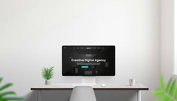 istock Modern desktop computer on minimalist desk with plant and coffee cup displaying creative digital agency website in dark mode, bright office interior 2244325683