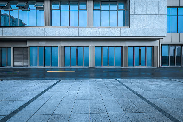 istock Empty stone pavement in front of a modern commercial building with large blue glass doors and windows after the rain. 2244326940