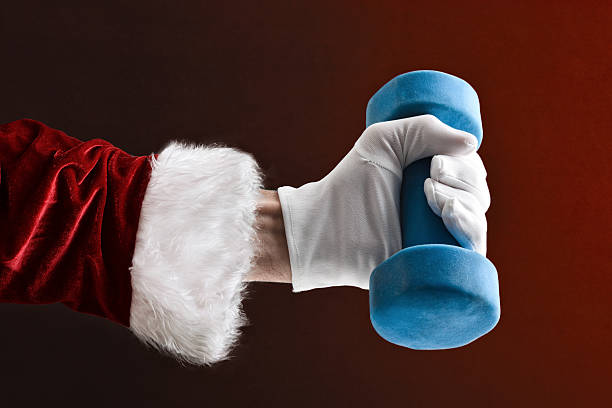 Santa Claus hand in suit and gloves lifting a blue dumbbell on red isolated background.