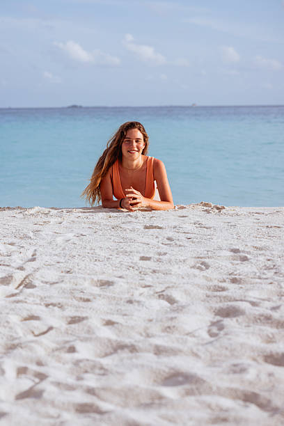 Young woman lying on white sand, enjoying a sunny beach day with turquoise ocean