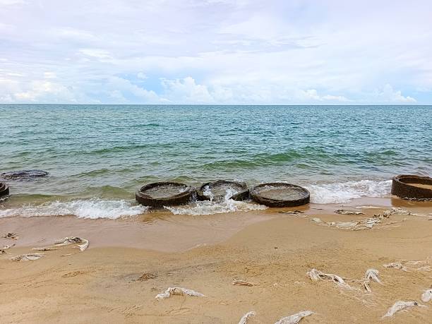 A tranquil coastal image showing weathered tires set along the sandy shore, used as waves breaker as gentle waves roll in. Ideal for themes of relaxation, nature, travel and outdoor getaways