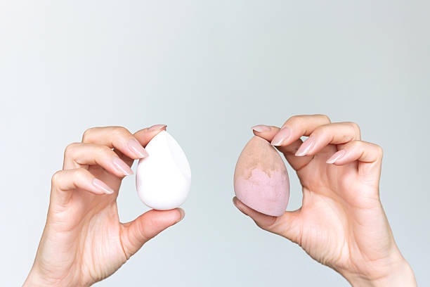istock A woman's hands holding a dirty and clear makeup sponges against a gray background.  Comparison make up sponges before and after. 2244339868