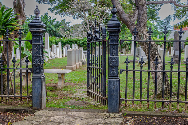 The ornate iron gate opens to a tranquil cemetery filled with historic tombstones and lush greenery, offering a peaceful place for reflection and remembrance