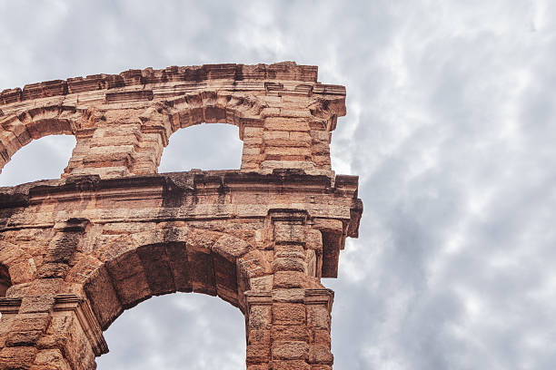 Minimal view of Verona Arena shows upper arches of Roman amphitheater rising against dense gray clouds, emphasizing its monumental form