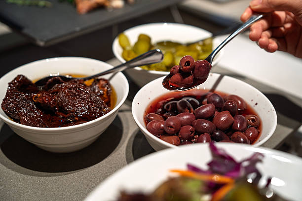 Person Scooping Black Olives from Bowl at Buffet Table