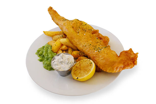 Stock photo shows a classic English fish supper featuring battered cod, golden chips, and mushy peas served in a cardboard takeaway box. This traditional fast food meal is a popular choice across the UK, known for its crispy texture and savory flavor