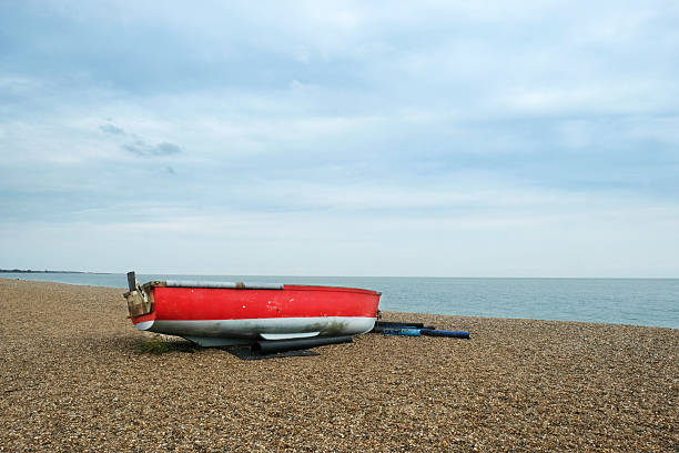 An old, red, small fishing boat moored on Dunwich Beach, Suffolk, UK