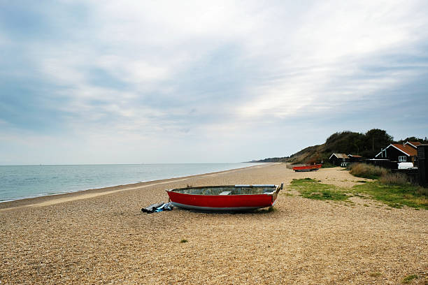 An old, red, small fishing boat moored on Dunwich Beach, Suffolk, UK