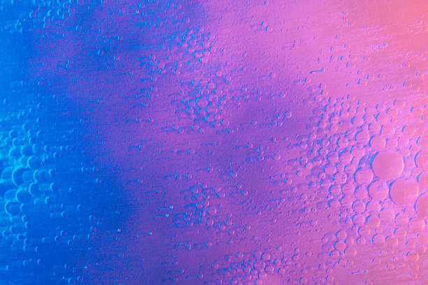 Macro abstract background of oil and water creating bubbles, illuminated by vibrant neon purple and pink/orange gradient lighting with long light streaks.