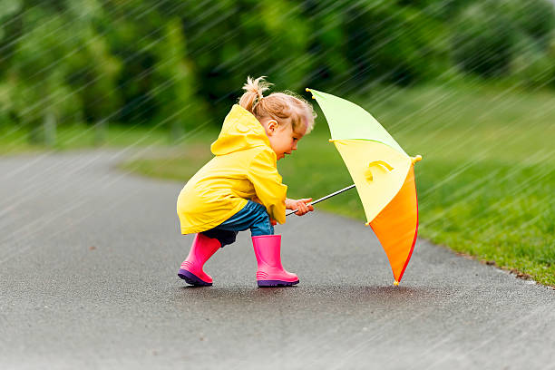 A Happy funny child with multicolored umbrella under the summer raining day