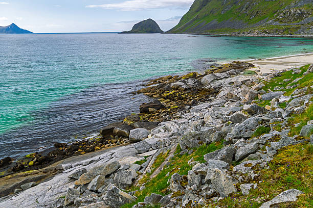 A rocky shoreline with a large body of water in the background in Norway. The rocks are scattered throughout the scene, with some closer to the water and others further away