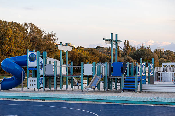 Expansive empty children's playground, showcasing multiple blue and teal play areas, slides, and climbing frames on sand, offering a vibrant space for youthful activity and joyful exploration