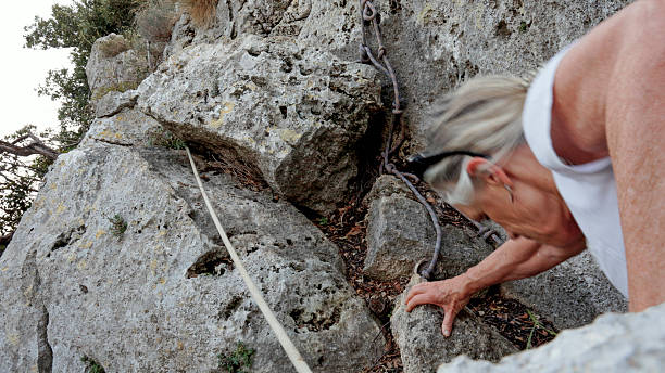 Senior woman scrambles up steep rock face with rope, maritime alps, Finale LIgure, Liguria