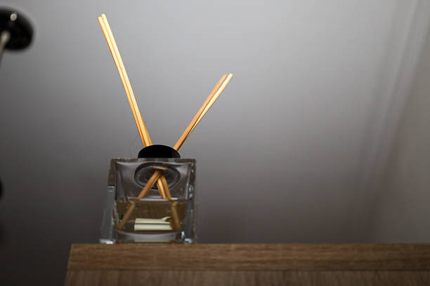 A glass square diffuser with aromatic oil and bamboo sticks stands on a wooden surface, creating a cozy accent in a modern interior.