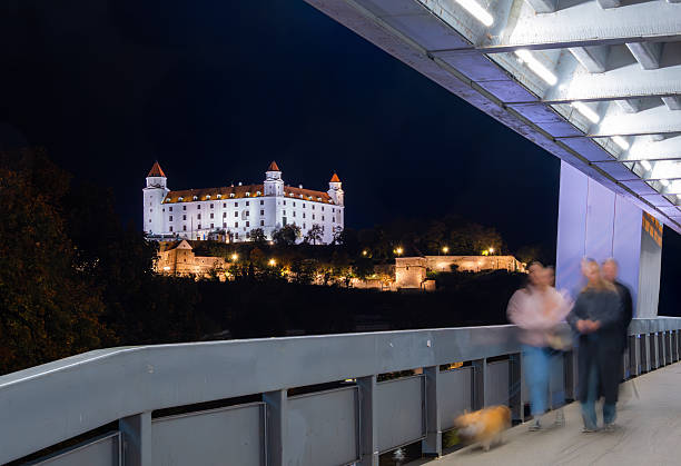 Night view of Bratislava Castle illuminated, framed by a modern SNP bridge.