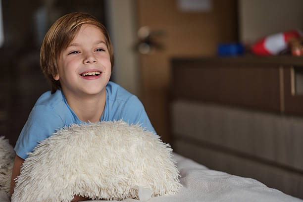 Young boy smiling joyfully while relaxing on a soft pillow in a bedroom