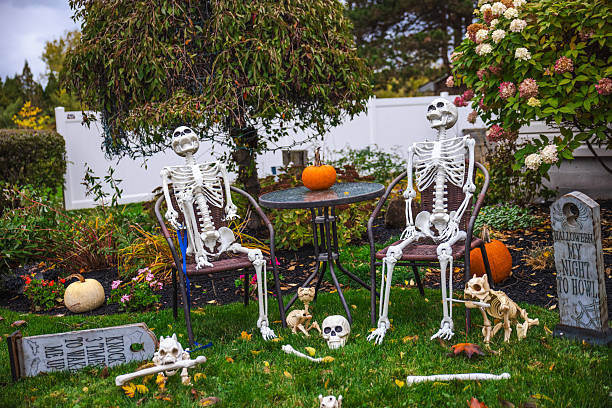 istock Two Halloween skeleton decorations sitting at a garden table with pumpkins, surrounded by tombstones and bones in a festive autumn yard. 2244402805