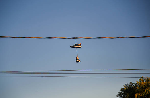 Colourful sneakers are flung across a power line under forboding skies.  Light grain.