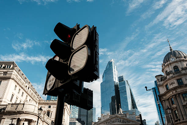 Traffic light standing prominently with a red signal, symbolizing flow and regulation against a backdrop of historic domed buildings and contemporary glass skyscrapers in the financial district