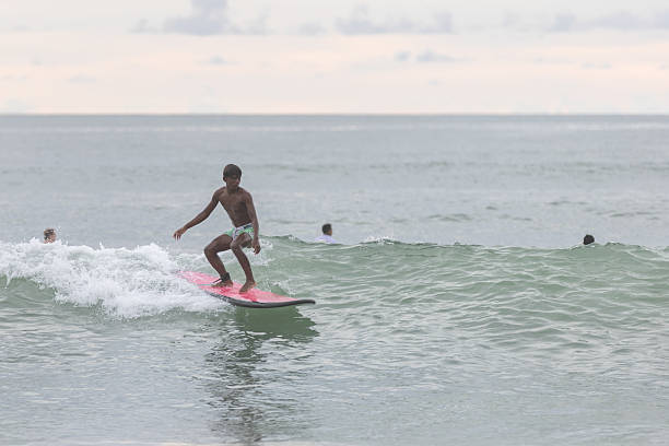 Black surfer man holding vintage surf board on the beach at sunset - Focus on face